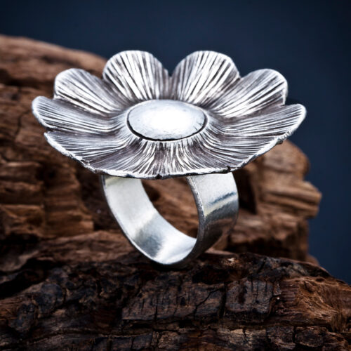 Fotografía de un anillo de plata con diseño de flor, capturado sobre madera en un estilo artístico por NUA Estudio.